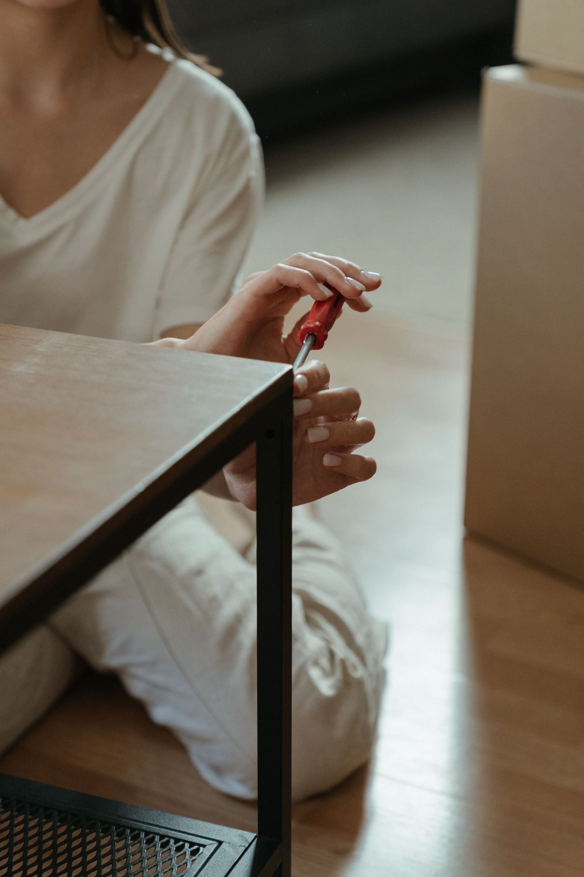 A woman using a screwdriver while assembling a table indoors.